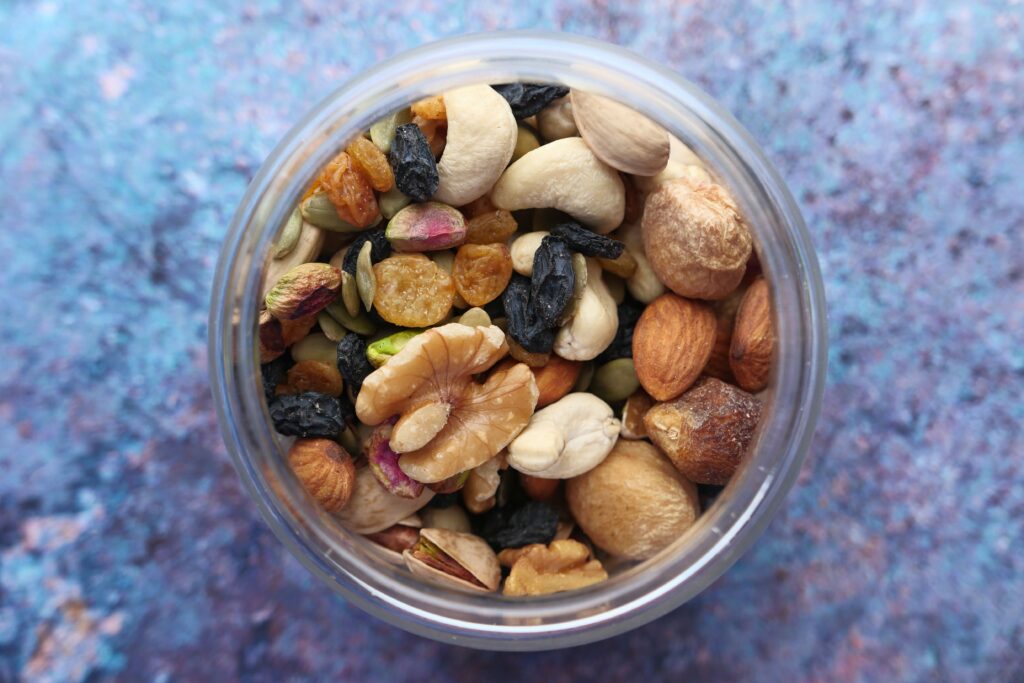 pexels-photo-11350074-11350074 Top view of a variety of nuts and dried fruits in a jar against a blue background.